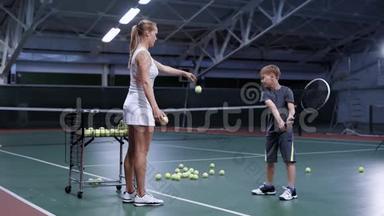 女子在<strong>网球场</strong>上与小男孩练习击球时抛球